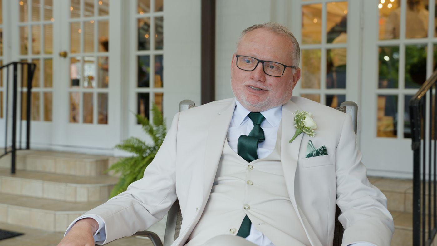 A wedding guest in a cream suit sharing a message during his interview